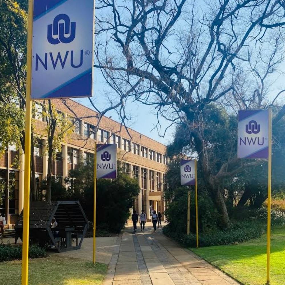 North-West University NWU Banners Along Walkway Students walk along a tree-lined path at North-West University beneath NWU branded banners.