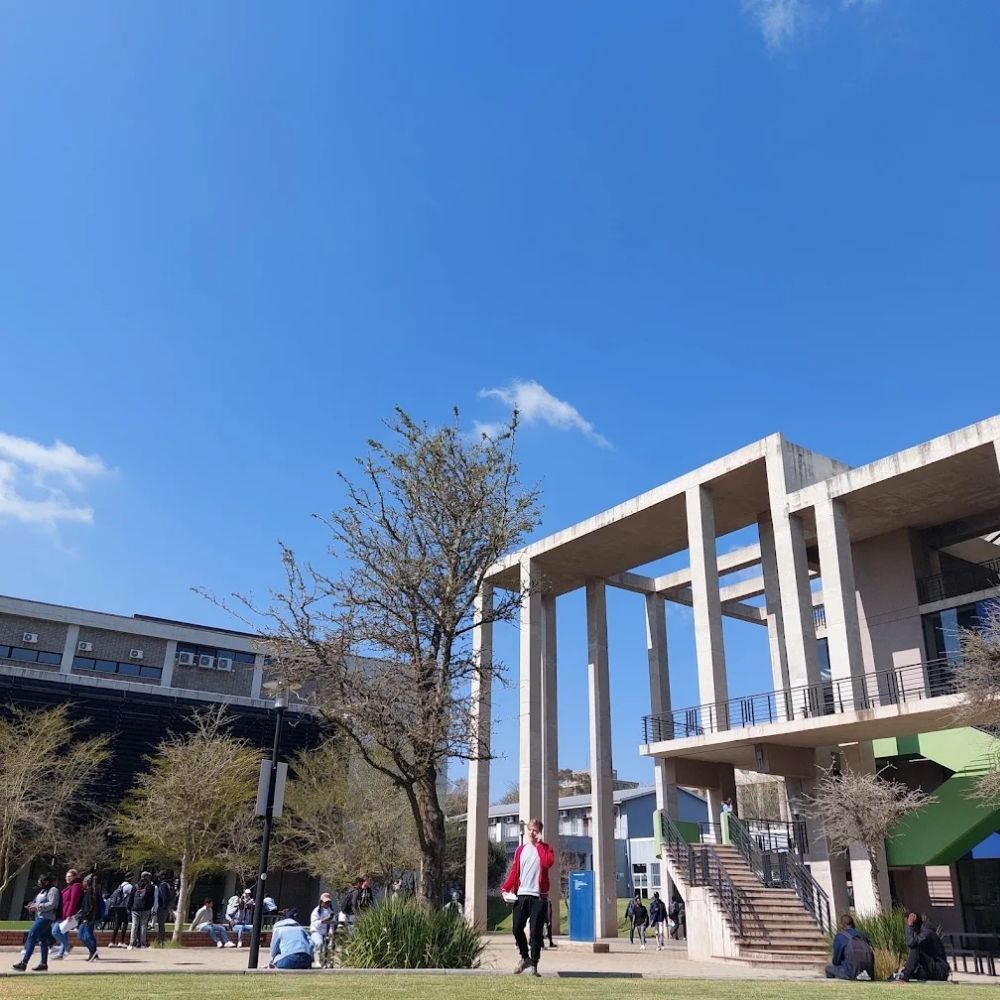 Students on an Outdoor Plaza at the University of the Witwatersrand Students walk and gather on a sunny plaza beneath a concrete structure at the University of the Witwatersrand.